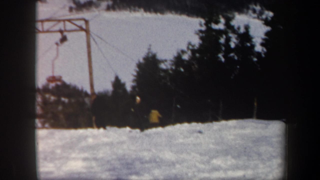 1962 Vermont home-movie frame showing a snow-covered ski slope, dark tree line, and visible ski lift hardware.