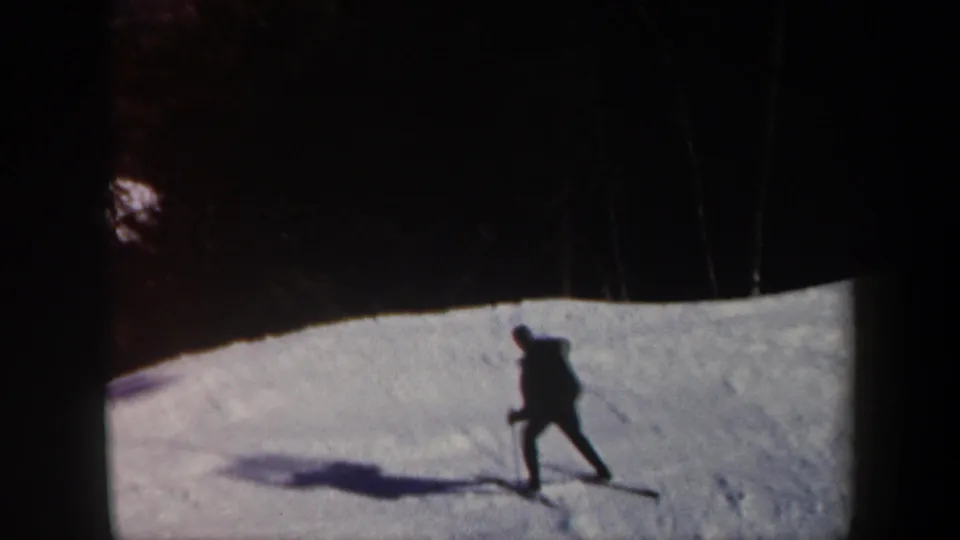 The lone skier continues downhill on a Vermont ski slope, silhouetted against bright snow and trees.