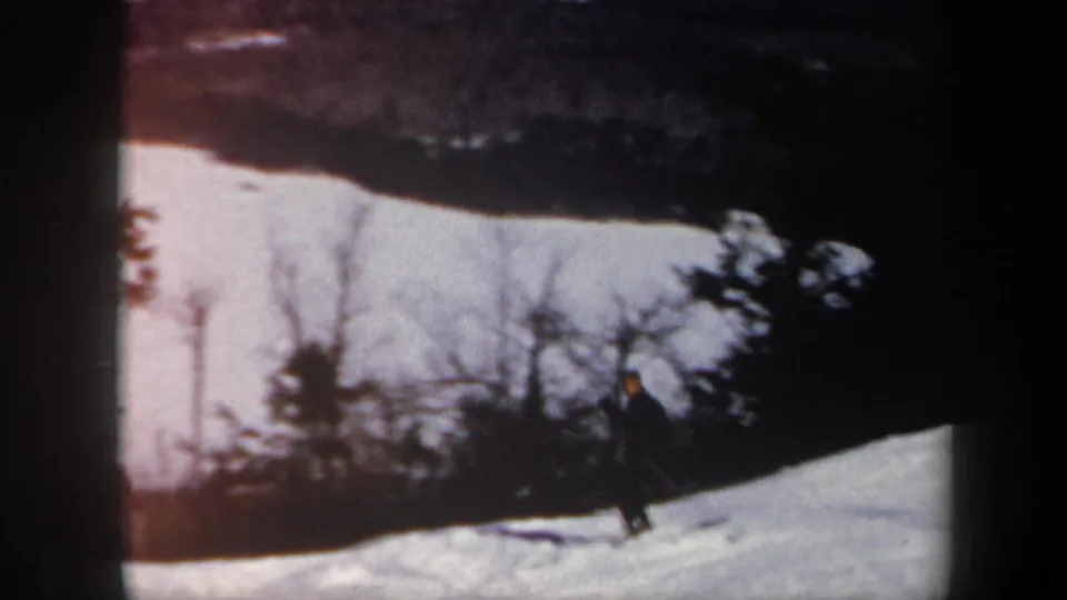 A distant skier crosses the lower part of the Vermont slope as trees and ski-area hardware sit in the background.
