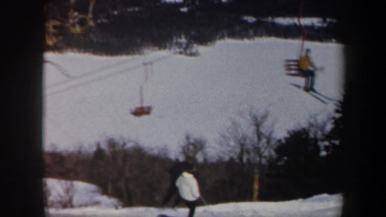 Person in a white jacket skis below a moving chairlift on a snowy hill.