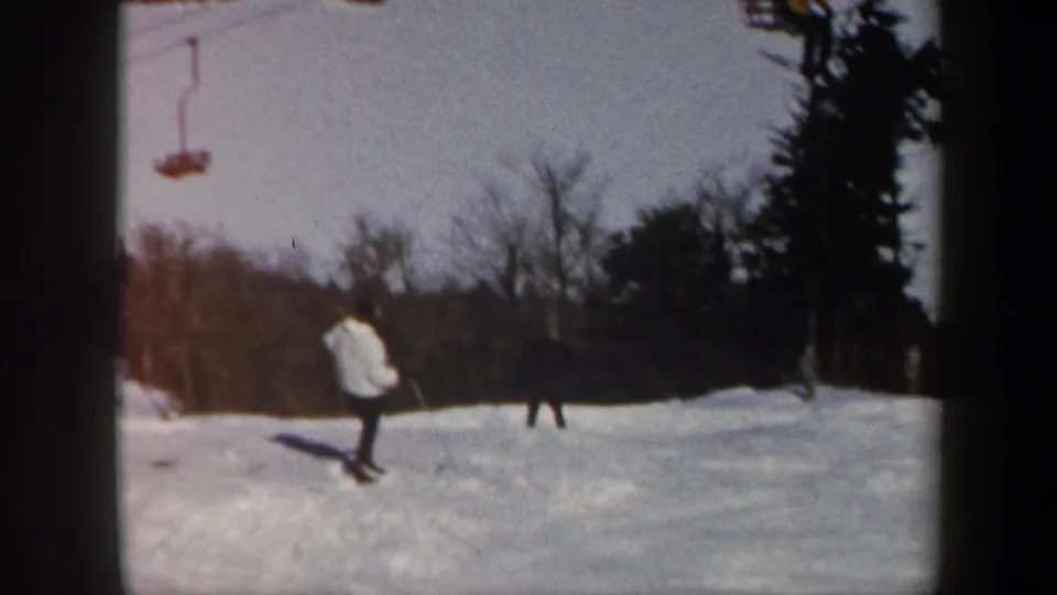 1962 Vermont frame showing two skiers on the resort slope with chairlift equipment above and winter trees behind.