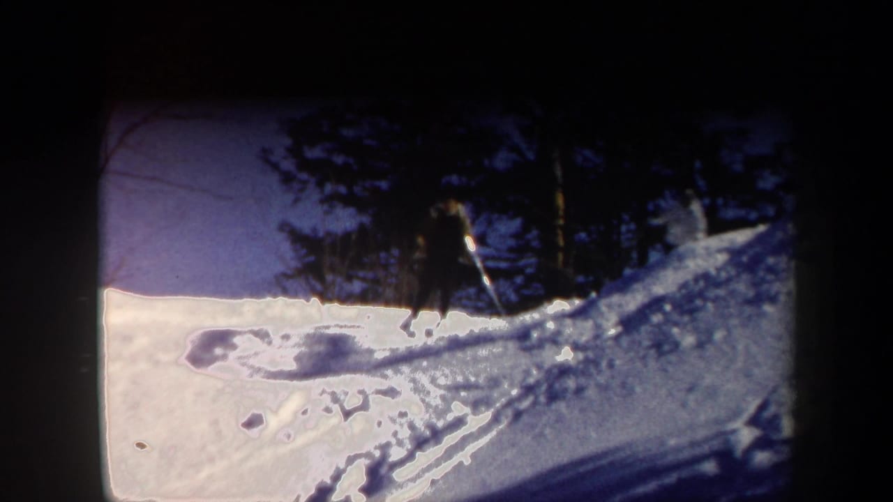 1962 Vermont home-movie frame showing a skier moving across a snowy slope below bare trees and evergreens.