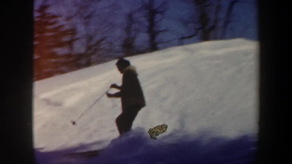 1962 Vermont home-movie frame showing a skier in dark winter clothing moving downhill through soft, grainy 8mm footage.