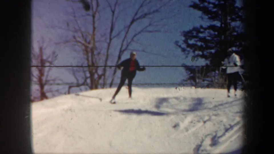 1962 Vermont frame showing skiers near a snowy rise, with a visible lift line or cable crossing the background.