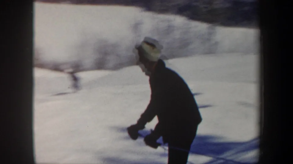 1962 Vermont 8mm frame showing a side view of a skier in a dark jacket crossing a bright snowy slope.