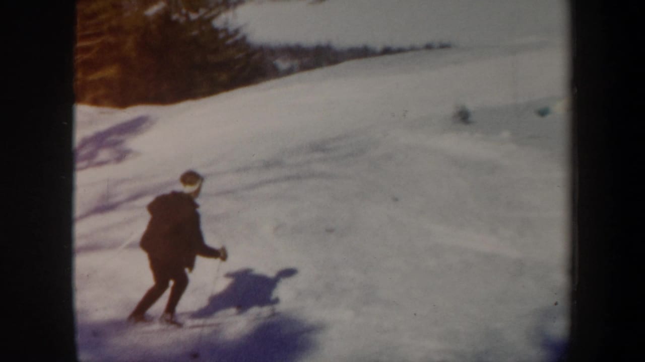 1962 Vermont home-movie frame with a skier moving across a snowy hillside, with trees and long shadows in the background.