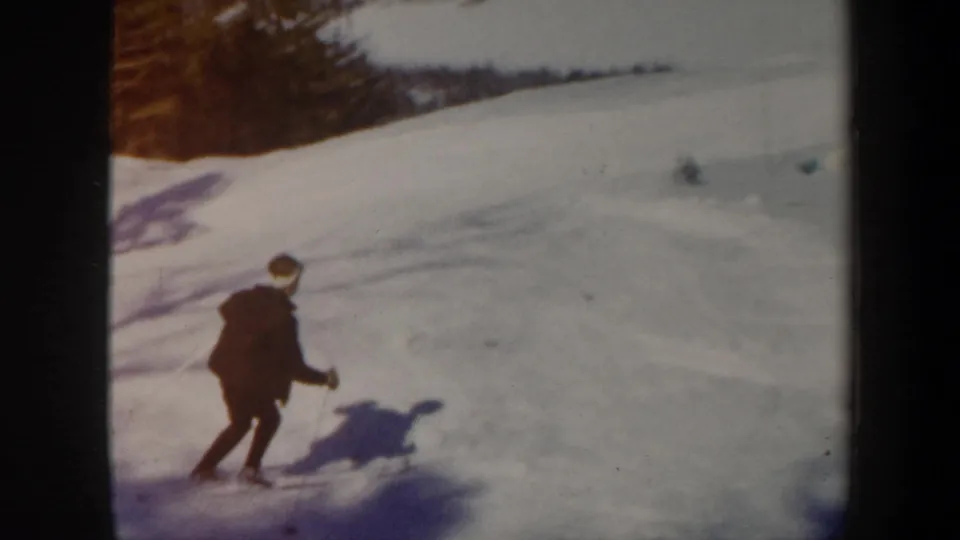 1962 Vermont home-movie frame with a skier moving across a snowy hillside, with trees and long shadows in the background.