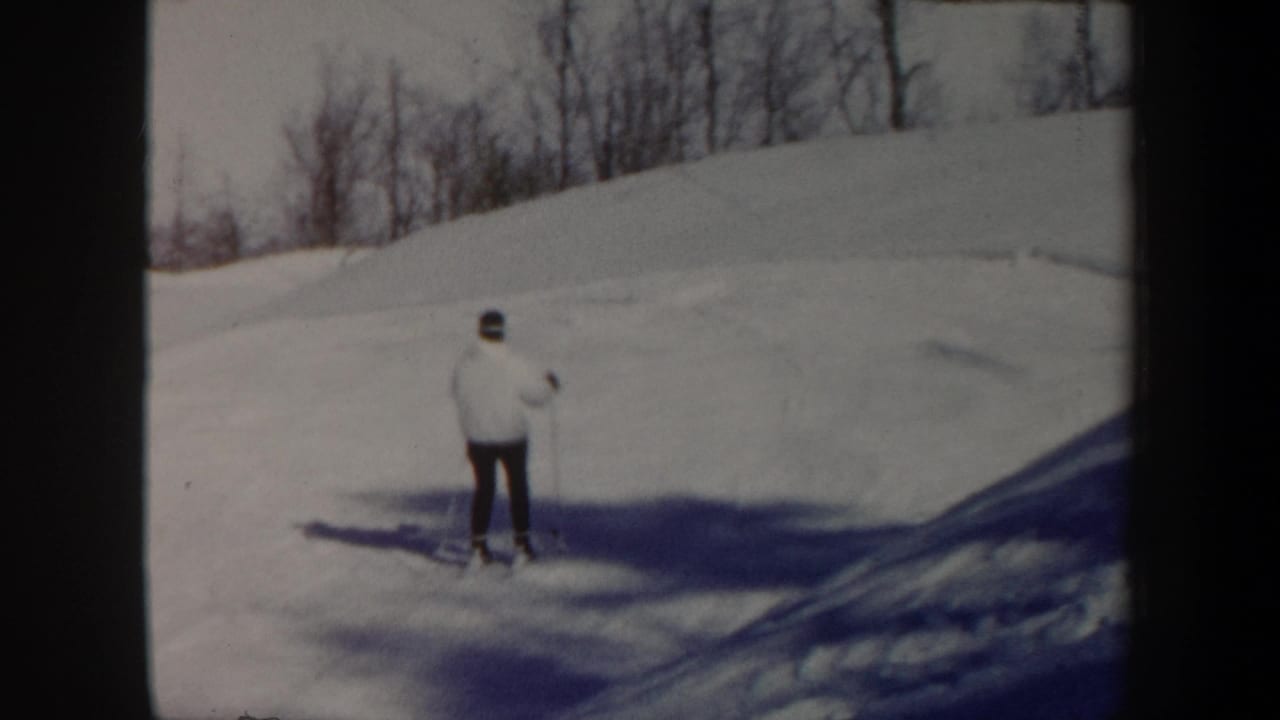 1962 Vermont 8mm frame showing a distant skier in a white jacket and dark pants on a snowy hillside lined with bare trees.