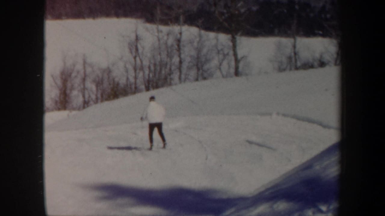 Distant skier moves across an open snowy hillside with trees at the ridge.