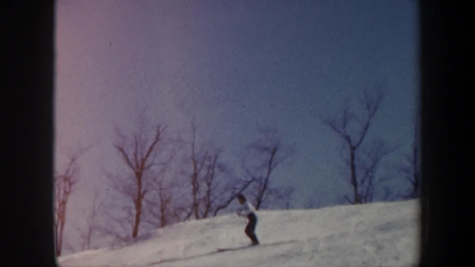 1962 Vermont home-movie frame showing a skier descending a snowy slope, with bare trees silhouetted against the sky.