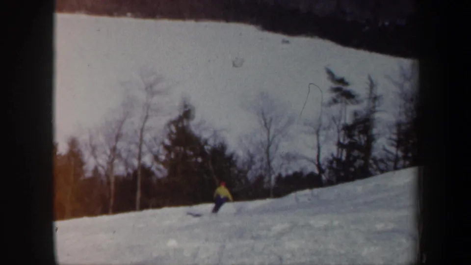 1962 Vermont 8mm frame showing a distant skier on a snow-covered hill, with bare trees and evergreens behind.