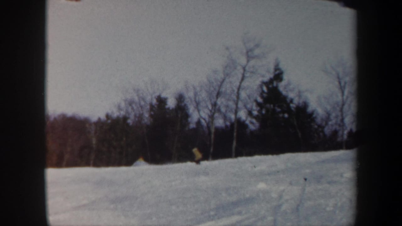 1962 Vermont 8mm frame showing a distant skier crossing a snow-covered slope below winter trees.