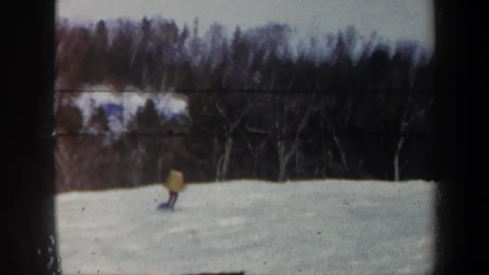 A skier in a pale jacket moves near the lower frame of a 1962 Vermont winter home movie shot.