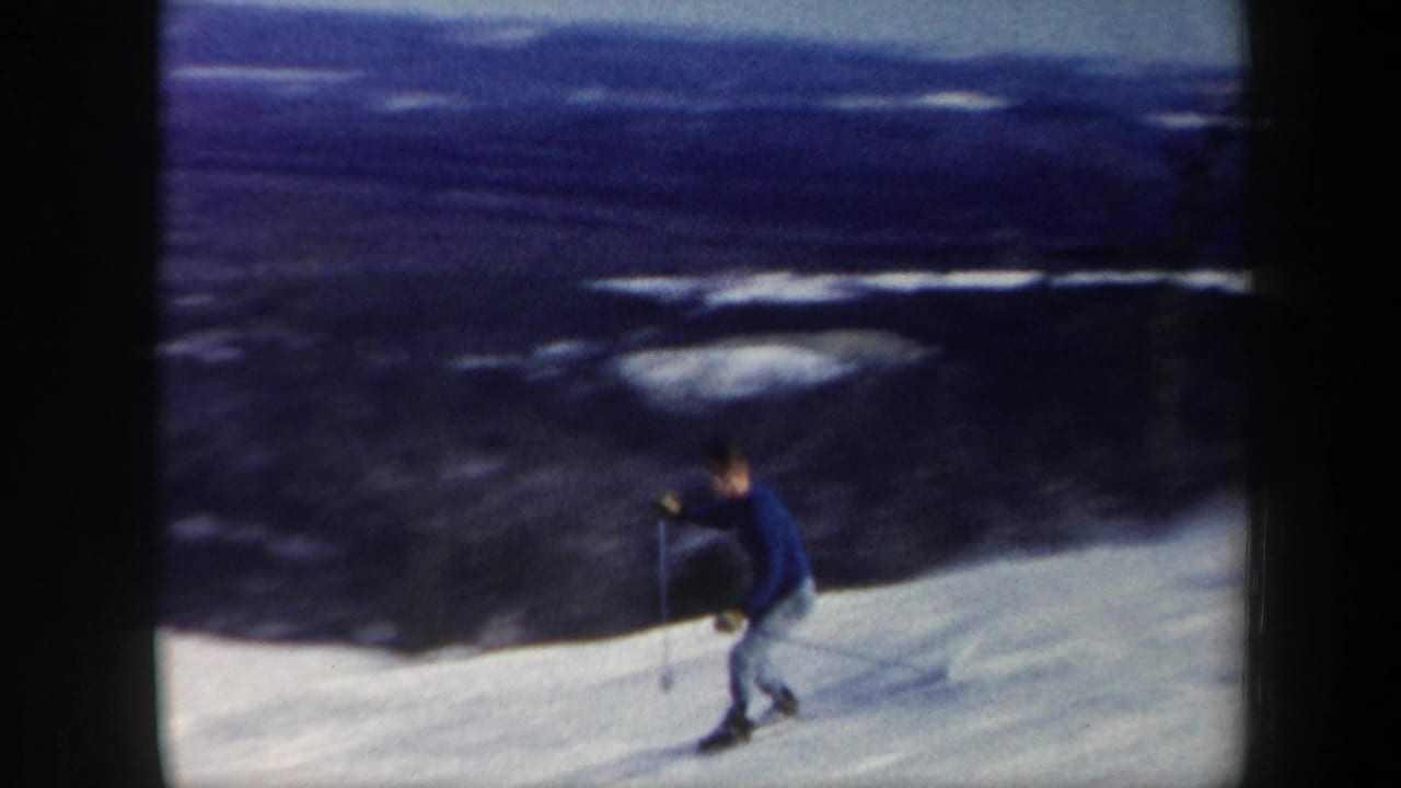 Skier descends a bright snowy slope with dark distant hills in the background.