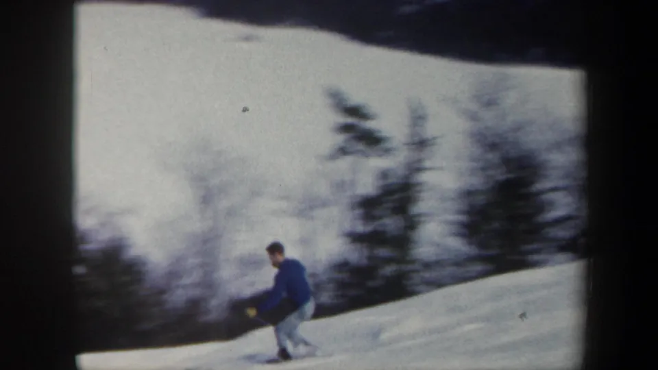 The skier continues across the Vermont snowfield, partially blurred by handheld 8mm motion and framed by winter trees.