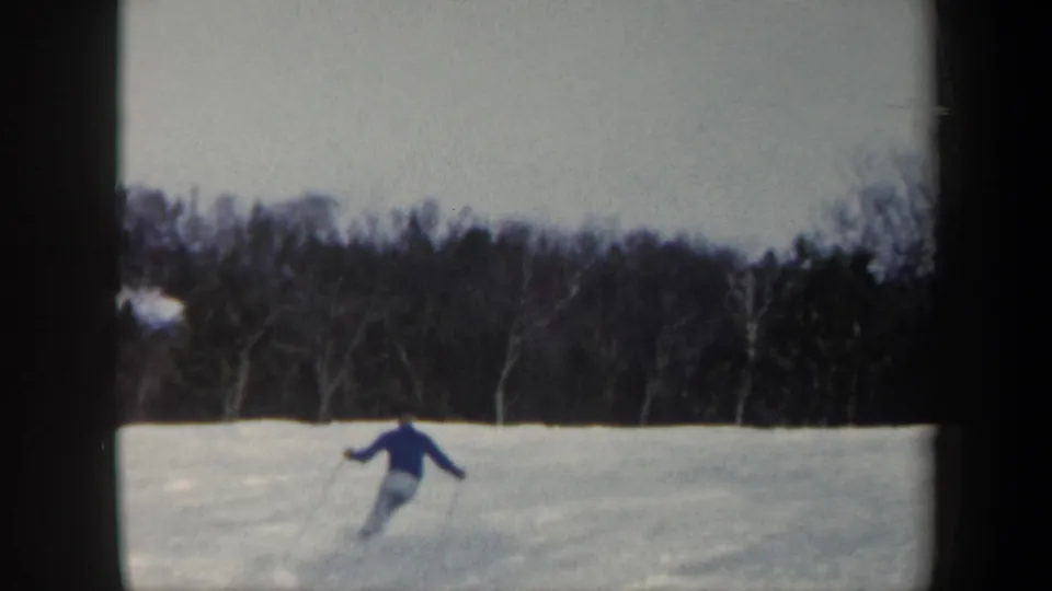 A wide 1962 Vermont frame shows the skier turning across an open snowy slope before a dark winter tree line.