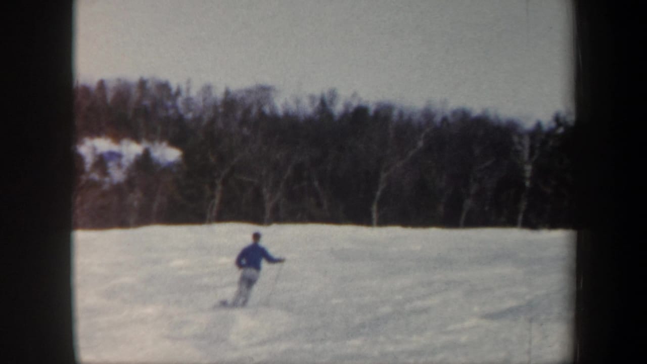 1962 Vermont 8mm frame showing a distant skier in blue moving across a snowy slope bordered by winter trees.