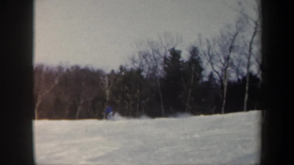 Late frame from the 1962 Vermont 8mm clip showing the skier in blue low on the snow near the wooded edge of the slope.