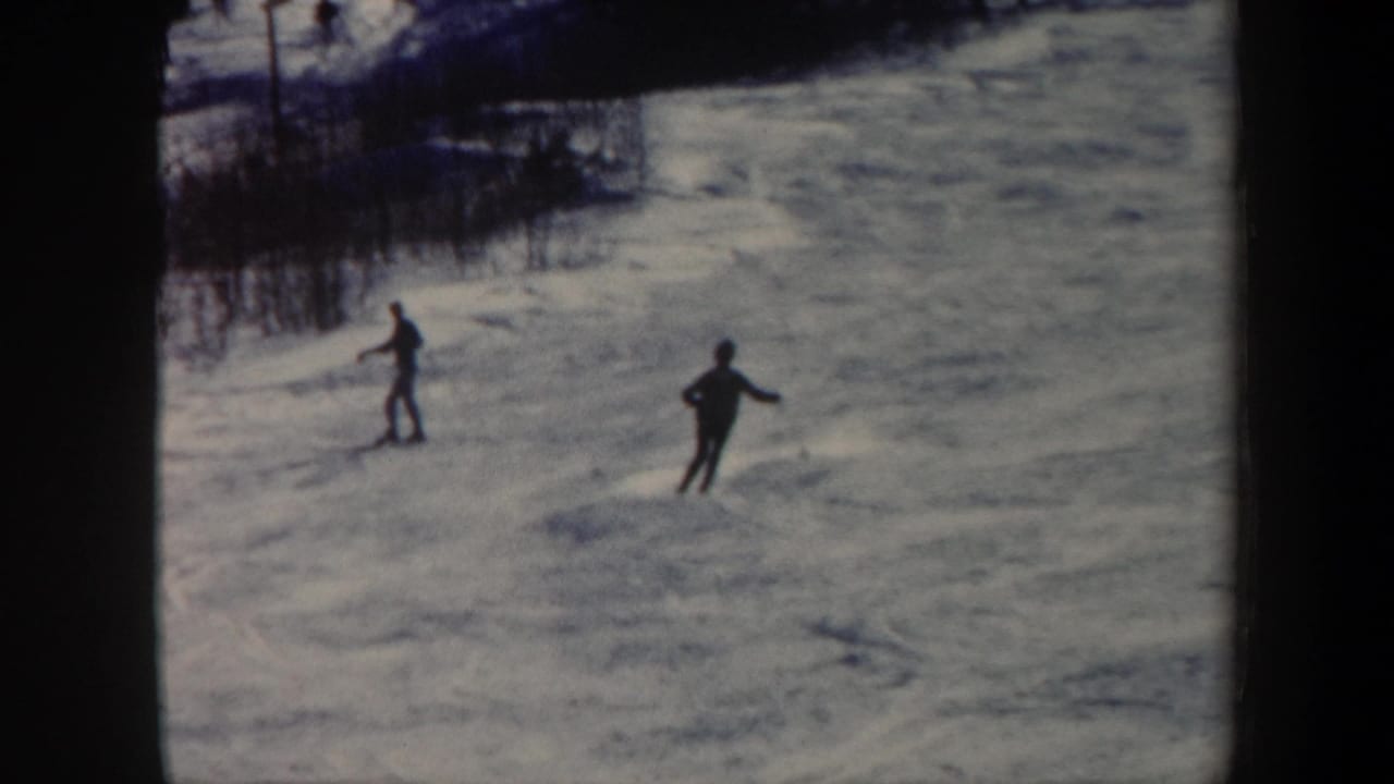 1962 Vermont 8mm frame showing two small silhouetted skiers crossing a bright snowy mountain slope.