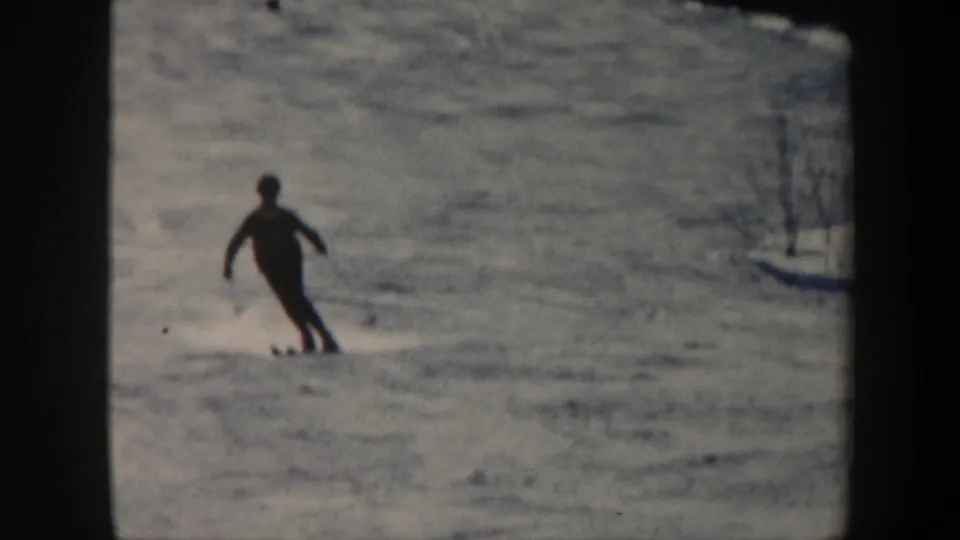 1962 Vermont 8mm frame showing one dark-clad skier carving across a bright, grainy snow slope.