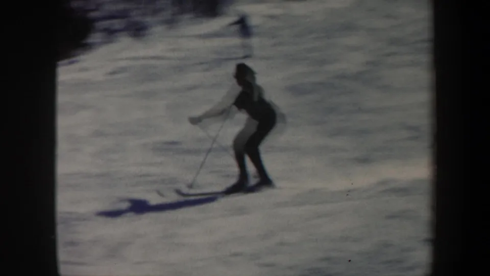 1962 Vermont home-movie frame of a silhouetted skier with poles gliding downhill across a snowy slope.