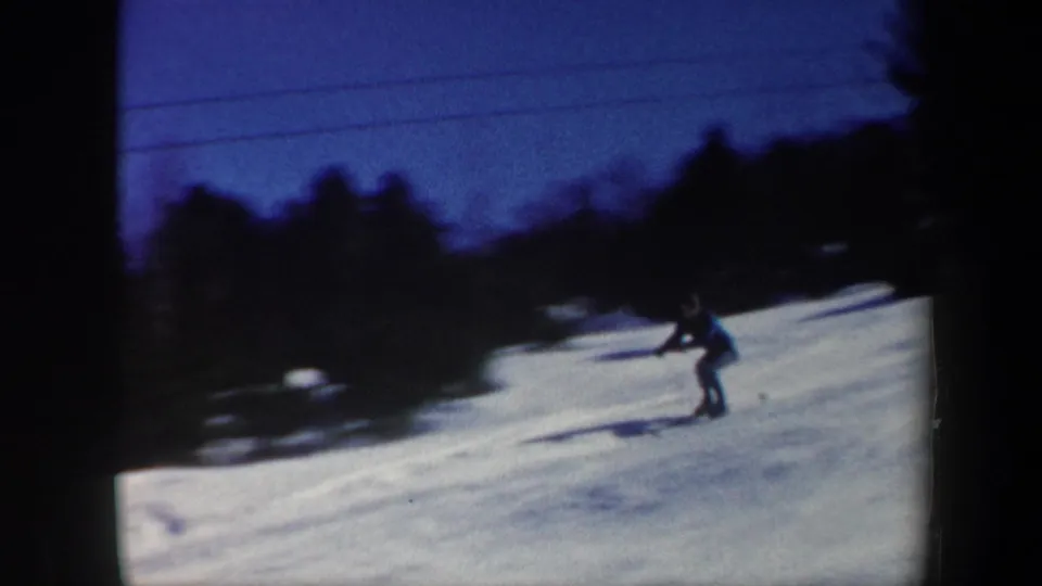 The home-movie camera catches a skier descending a snowy Vermont slope, with soft focus, deep shadows, and trees behind the run.