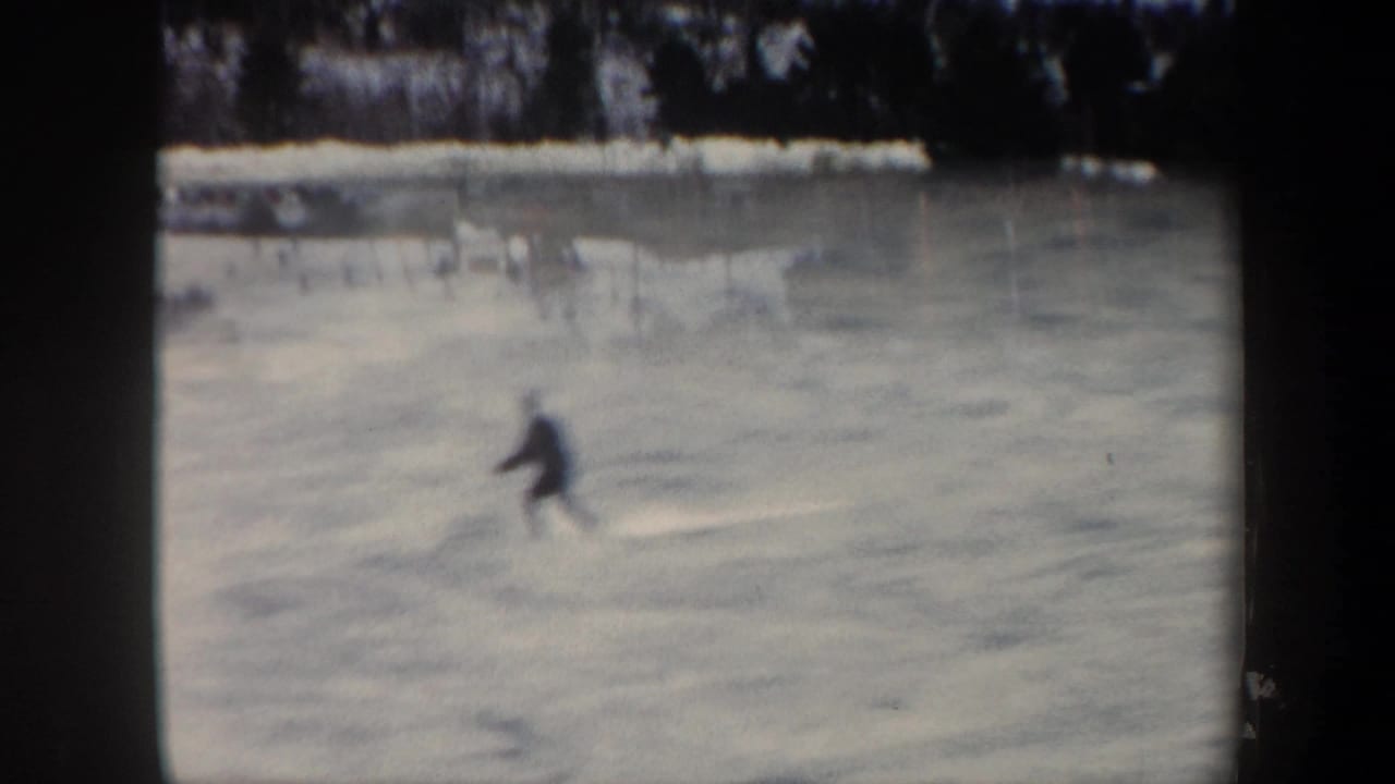 Distant skier crossing a pale snowy slope bordered by trees.