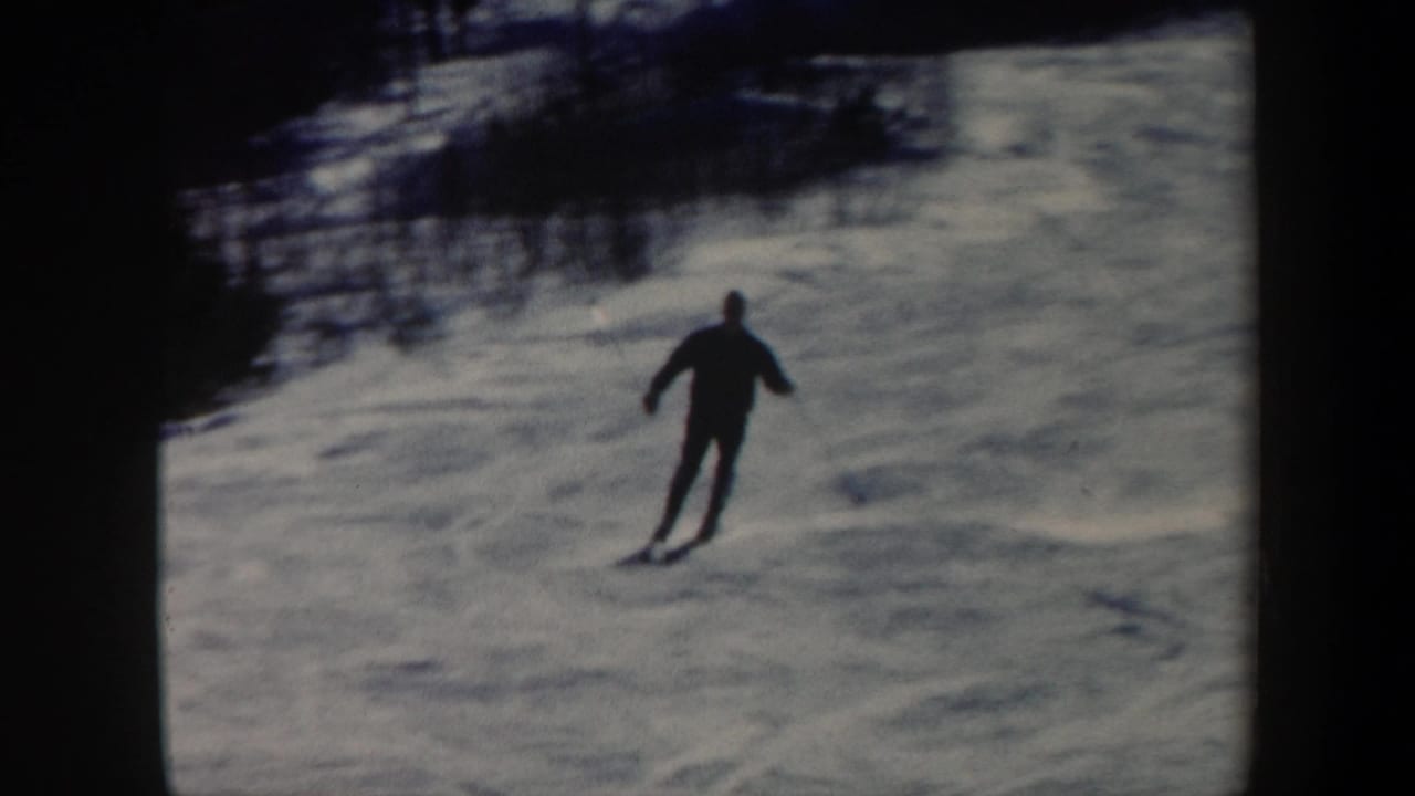1962 Vermont 8mm frame showing an adult skier in dark winter clothing moving downhill on a snowy slope.
