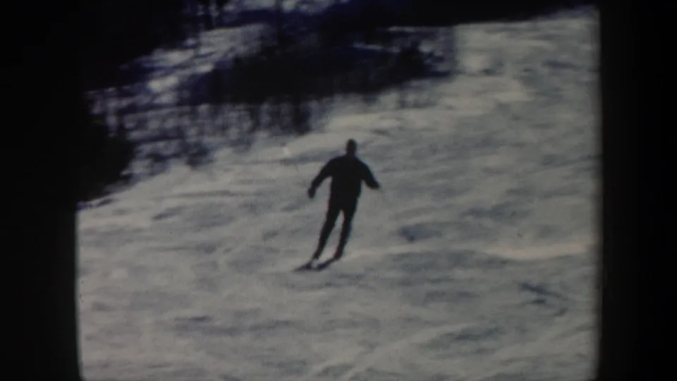 1962 Vermont 8mm frame showing an adult skier in dark winter clothing moving downhill on a snowy slope.