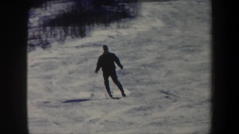 Adult skier in dark clothing glides across a Vermont snow slope in soft 8mm color footage.