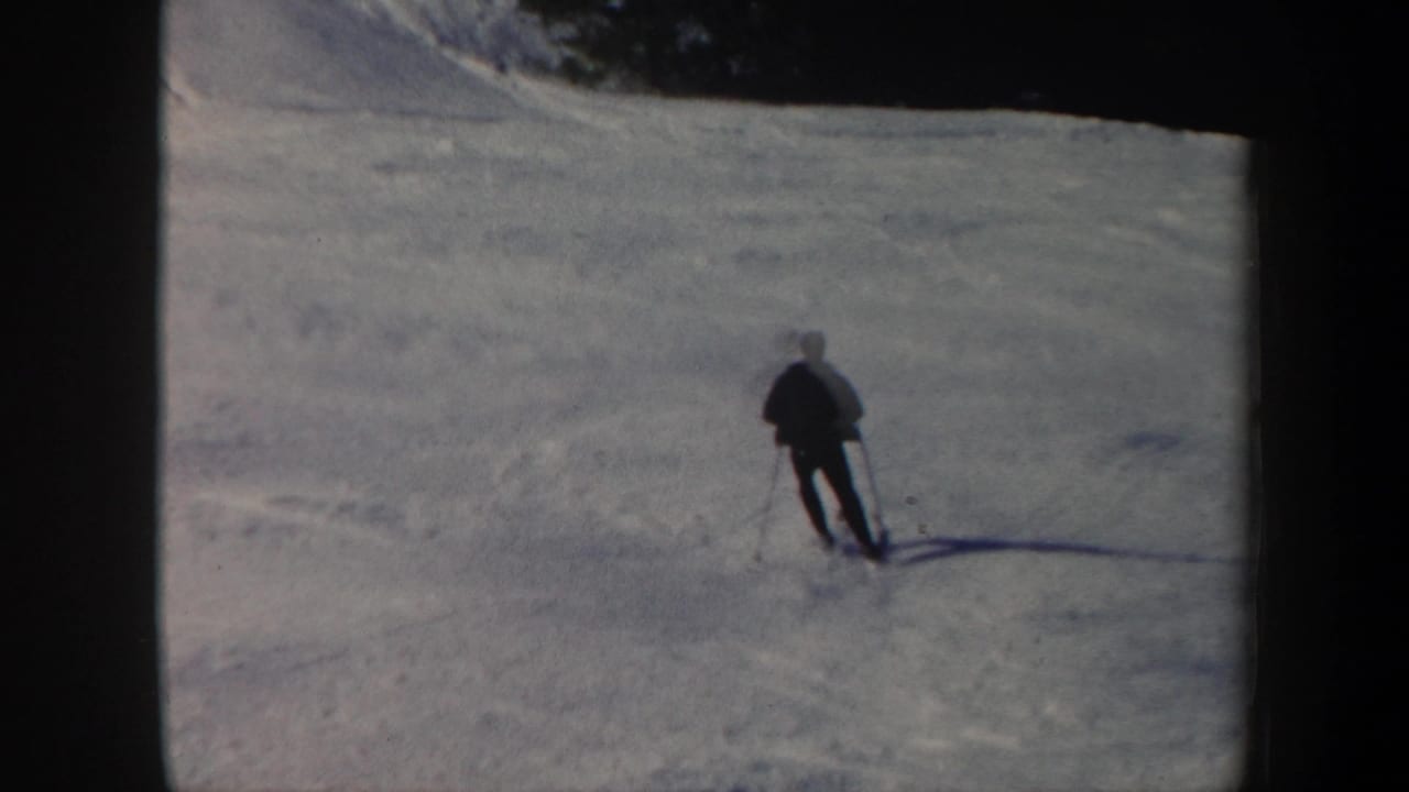 1962 Vermont 8mm frame showing a lone skier descending a snow-covered slope below a dark tree line.