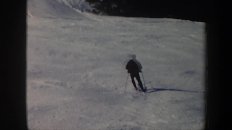 1962 Vermont 8mm frame showing a lone skier descending a snow-covered slope below a dark tree line.