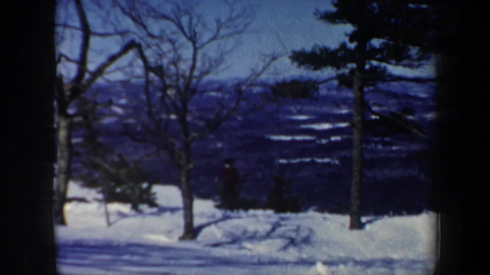 Vermont winter mountain view with snow-covered ground, bare branches, evergreens, and distant hills in 1962 8mm footage.