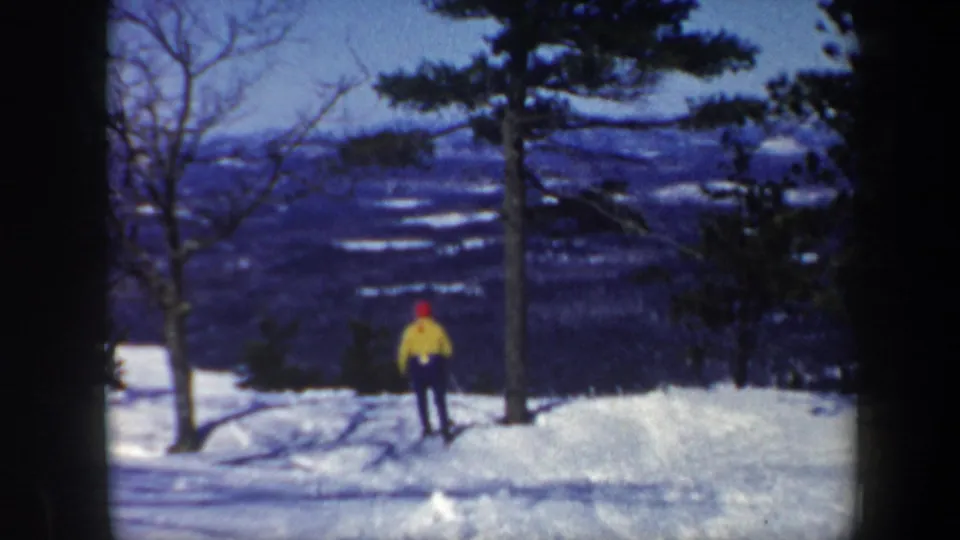 1962 Vermont 8mm frame with a distant skier in a yellow jacket and red hat among snowy trees and ridges.