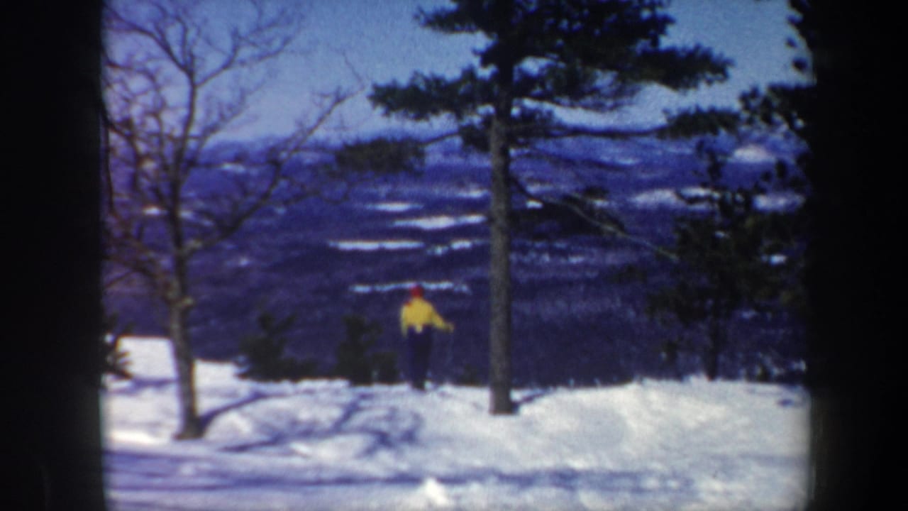 1962 Vermont home-movie frame showing a skier in bright outerwear on a snowy ridge with trees and a distant valley beyond.