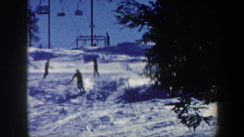 1962 Vermont ski slope scene with multiple distant skiers, tracked snow, trees, and chairlift equipment in the background.