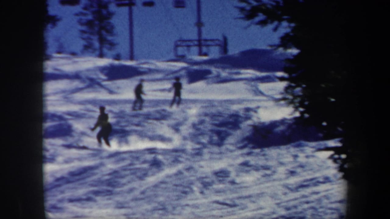 1962 Vermont home-movie frame showing skiers spread across a snowy downhill run with a ski lift structure in the background.