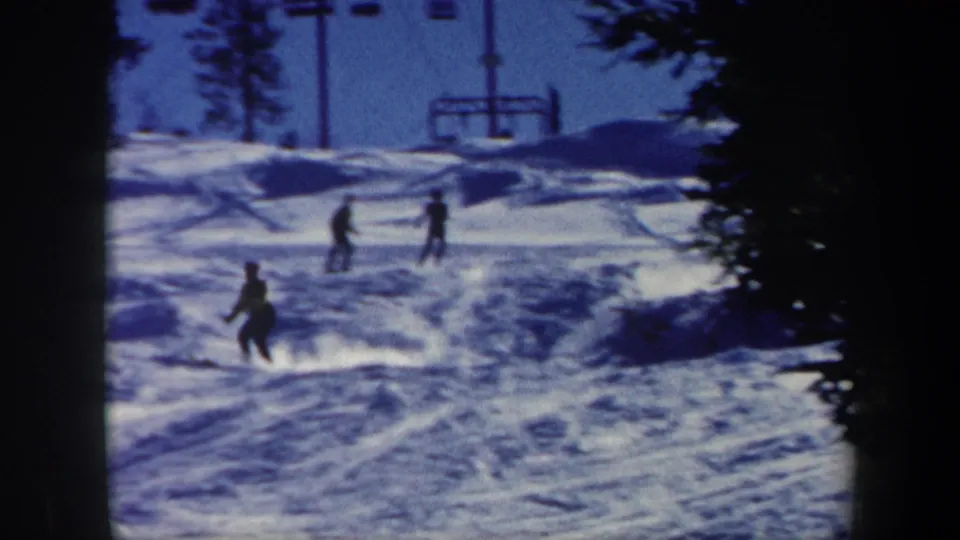 1962 Vermont home-movie frame showing skiers spread across a snowy downhill run with a ski lift structure in the background.
