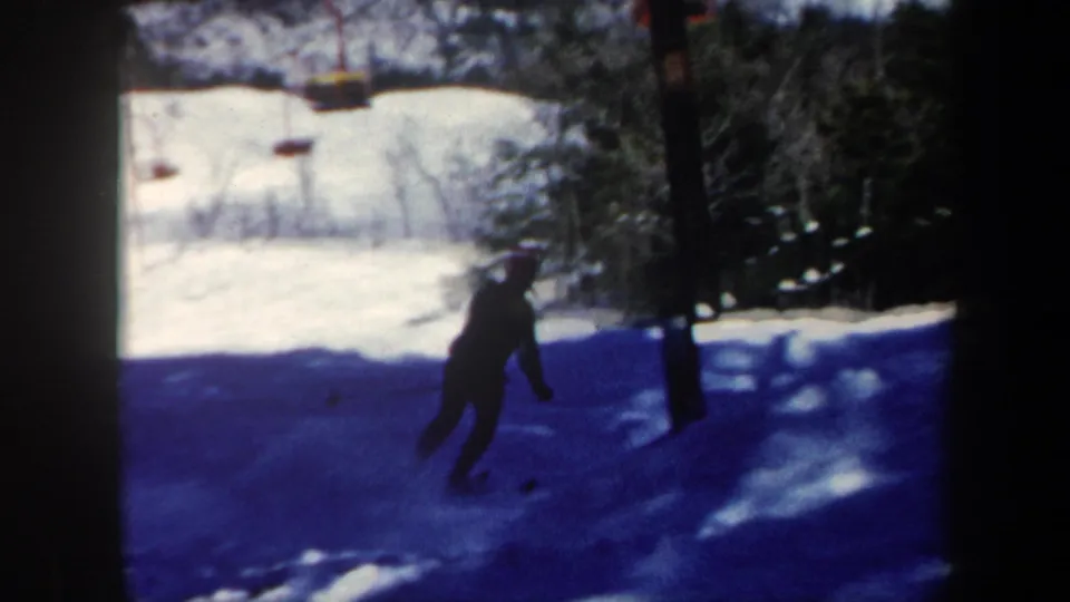 A dark-clad skier descends a Vermont snow slope, framed by evergreen trees and strong blue winter shadows.