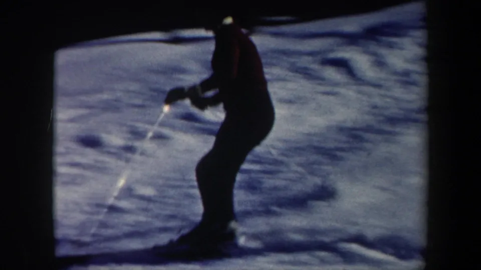 A silhouetted skier crosses a blue-shadowed Vermont slope, with soft focus and exposure shifts typical of 8mm home movies.