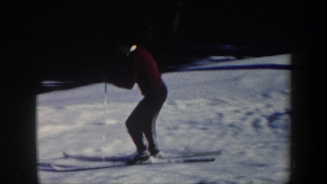1962 Vermont home-movie frame showing a skier in a red sweater and dark pants moving across snow near a wooded edge.