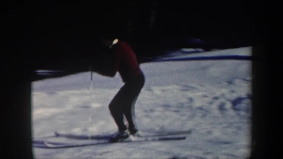 1962 Vermont home-movie frame showing a skier in a red sweater and dark pants moving across snow near a wooded edge.