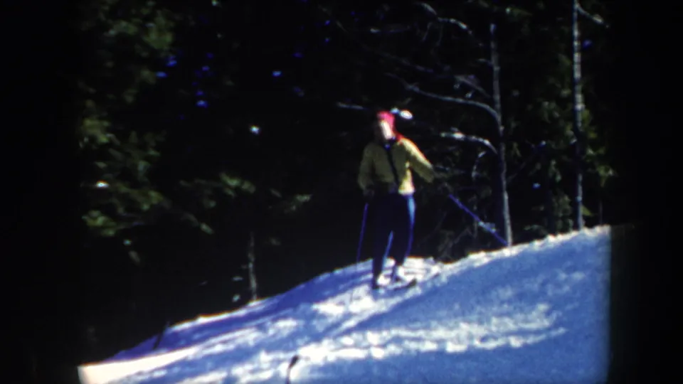 1962 Vermont winter frame showing a skier on a snow-covered rise, with poles and evergreen trees in the background.