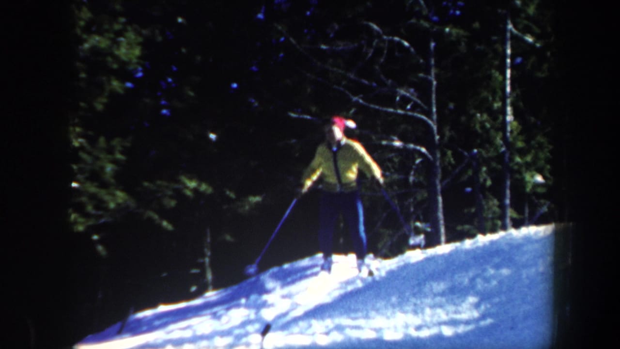 1962 Vermont 8mm frame showing a skier in a yellow jacket and red hat using poles on a snowy forest slope.