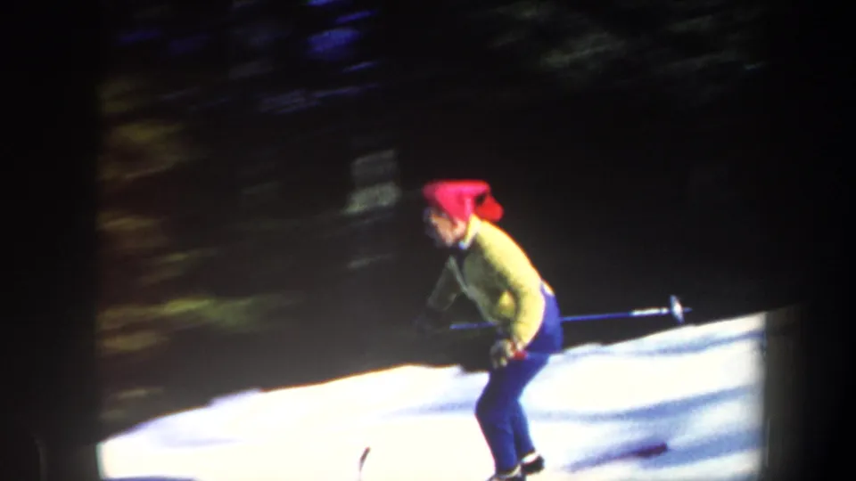 1962 Vermont 8mm frame showing a side view of the skier passing across the snow with dark trees behind.