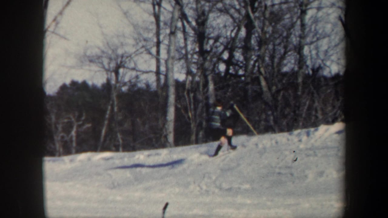 A skier in dark clothing moves near the crest of a snowy hill.