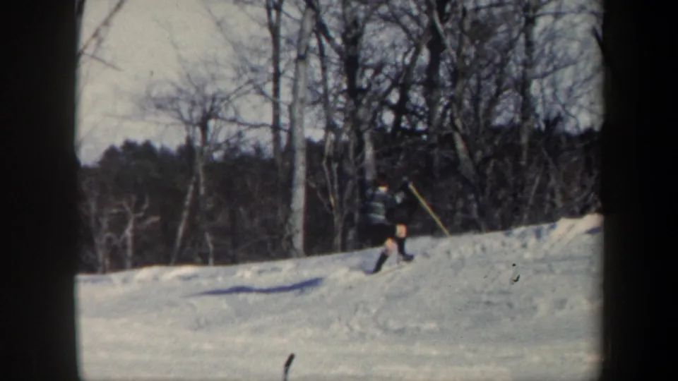 A distant skier appears near the top of a Vermont snow slope, framed by winter trees and 8mm gate edges.
