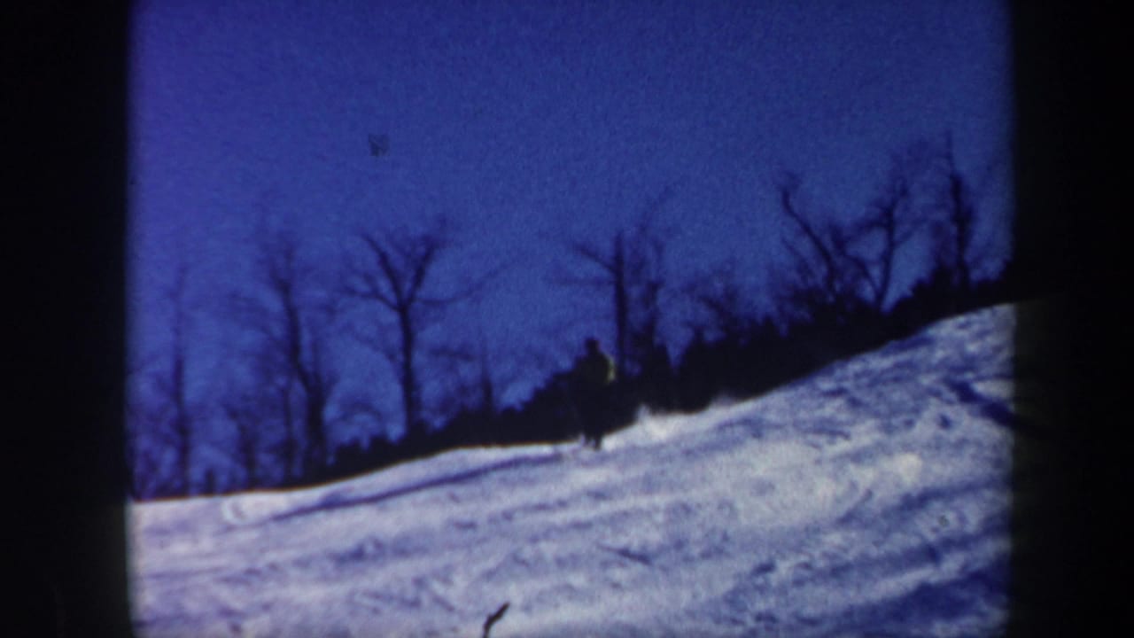 1962 Vermont 8mm frame showing a distant skier descending a snowy hillside at dusk with bare trees silhouetted behind.