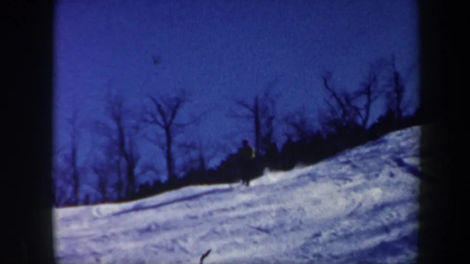 1962 Vermont 8mm frame showing a distant skier descending a snowy hillside at dusk with bare trees silhouetted behind.