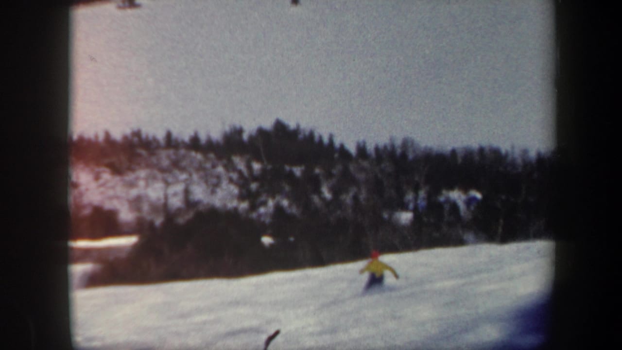 The skier appears farther down the open Vermont ski slope, framed by a dark wooded hillside and pale winter sky in 1962 8mm footage.